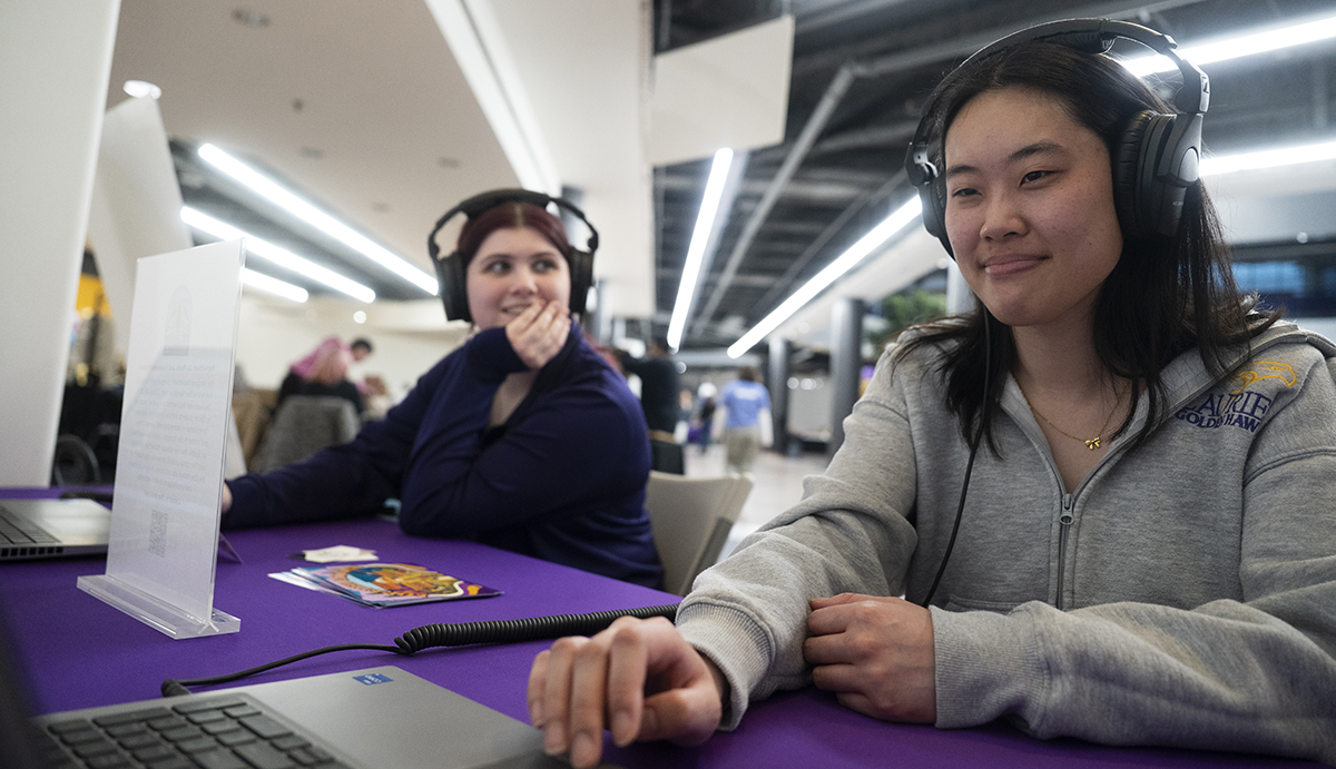 Two Laurier students listen to the MarketFest podcast on headphones